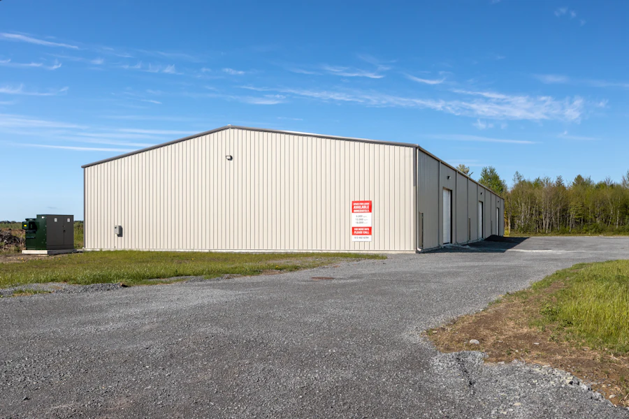 Pale steel warehouse beside a gravel truck court under a blue sky